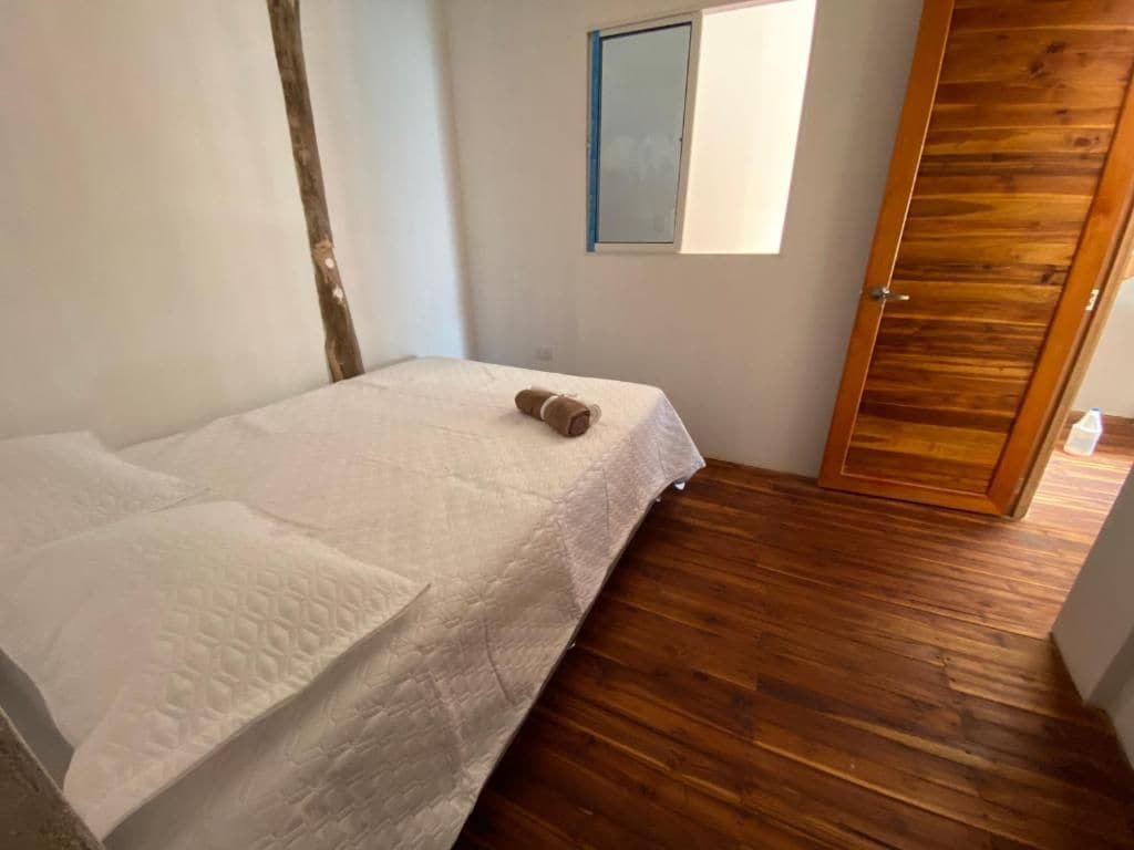 Un dormitori amb llit, terra de fusta, finestra i porta.