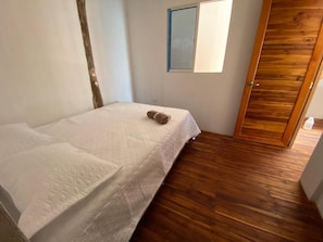 A bedroom with a bed, a wooden floor, a window, and a door. - Roma beach (Cartagena)