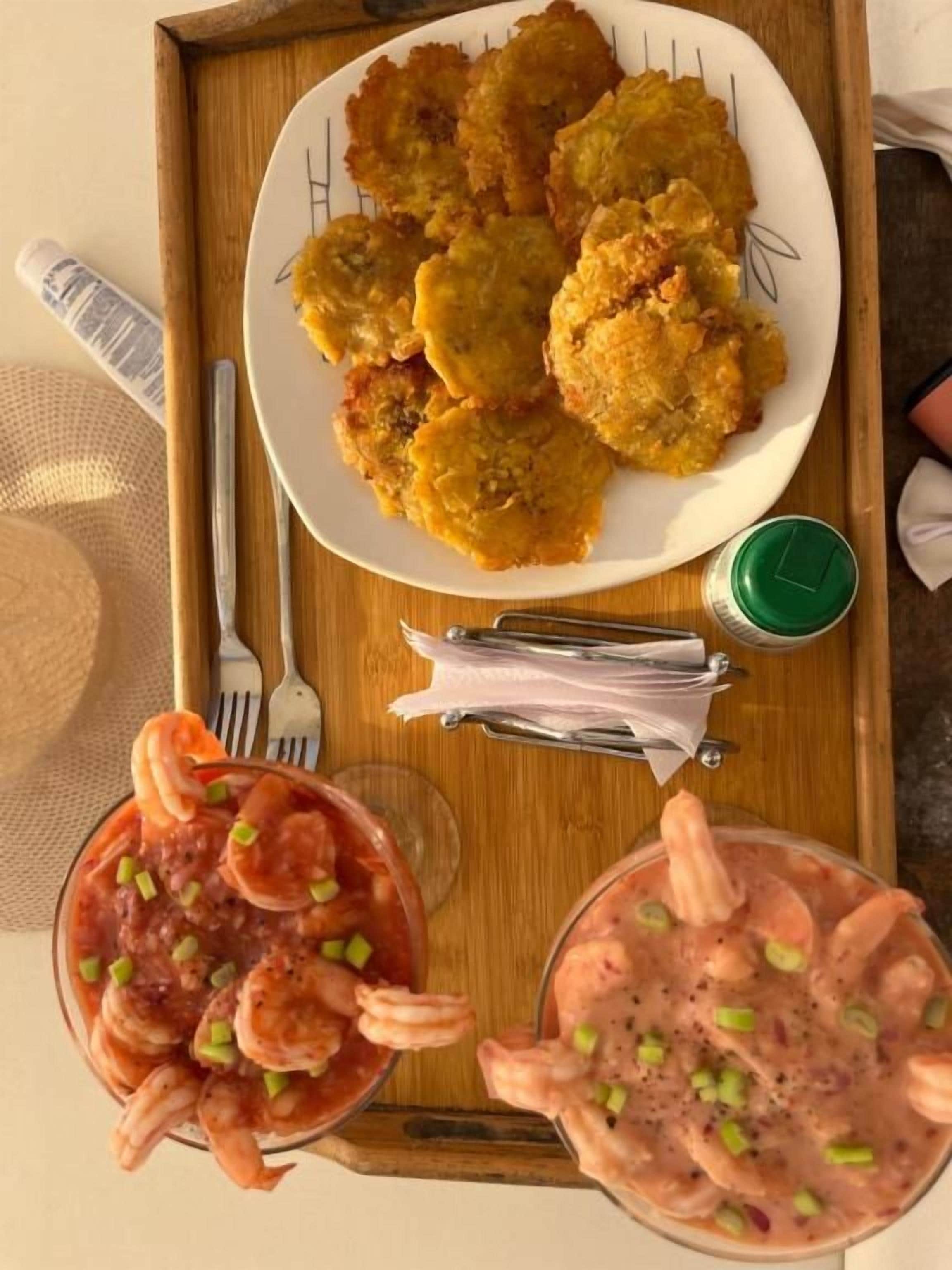 Una bandeja con una fuente de comida frita, dos vasos de sopa de camarón y un recipiente para salsa verde.
