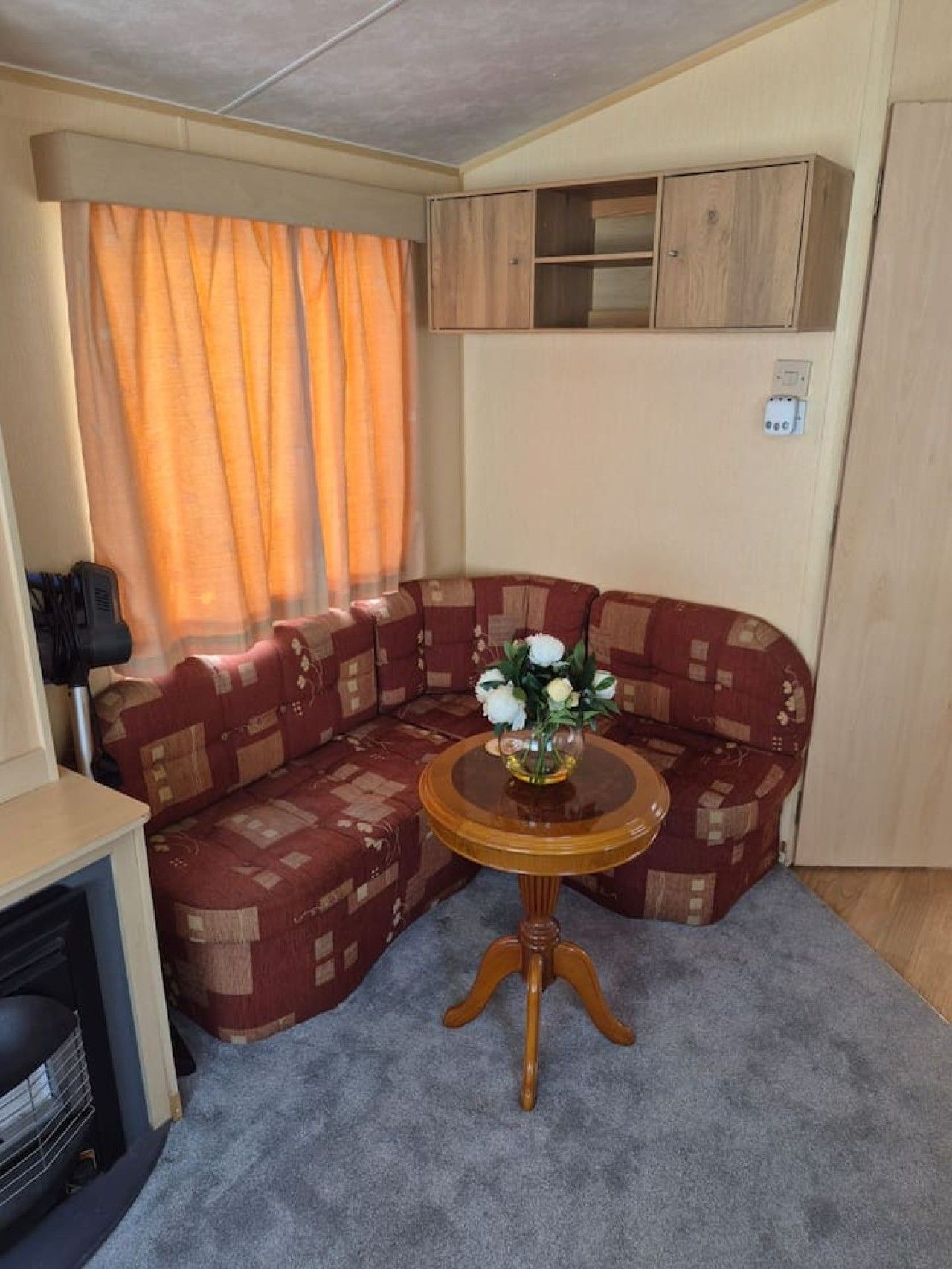 A compact living space with a sectional sofa, a small round table with a vase, and a heater.