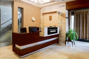 A reception desk with a sign reading 'TOWNHOUSE Company Serviced.' A clock, a fan, and a potted plant are visible.