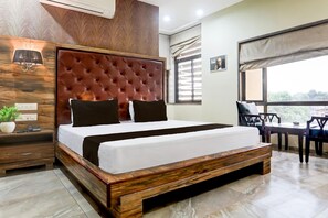 A modern bedroom with a large bed, wooden headboard, bedside tables, a small plant, and a view through a window.