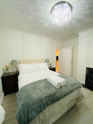 A neatly made bed with a grey bedspread and white pillows, a bedside table with a lamp, and a chandelier on the ceiling. - Red Brick Haven 5Bed 2Bath for Memorable Reunions (Isle of Wight)