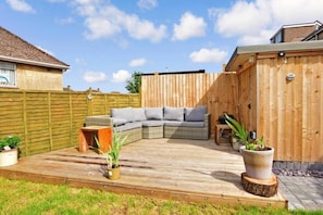 A wooden deck with a built-in sectional sofa, potted plants, and a wooden fence. - Red Brick Haven 5Bed 2Bath for Memorable Reunions (Isle of Wight)