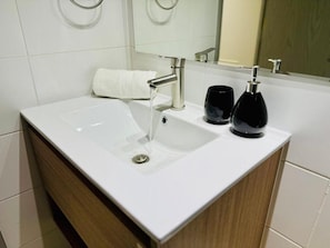 Un baño con un lavamanos blanco, un espejo y dos dispensadores de jabón negros.