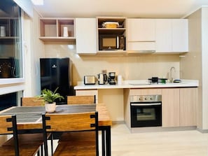 Cocina compacta con microondas, estufa y lavabo. Hay una mesa de comedor con sillas y una planta en maceta.