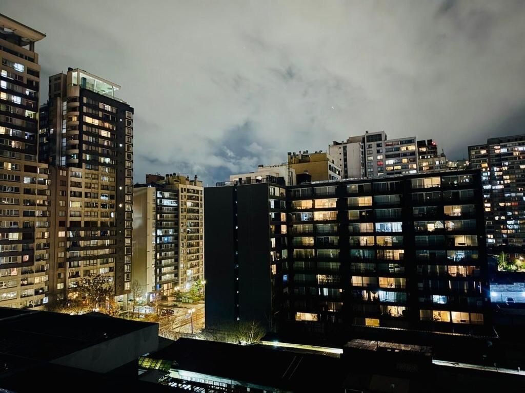 A nighttime cityscape with high-rise buildings, some with illuminated windows, under a cloudy sky.