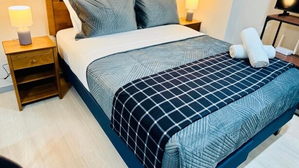 Hotellihuone, jossa on sänky, kaksi yöpöytää, televisio ja sängyllä rullalle taitettu pyyhe.