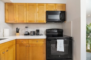 A kitchen with wooden cabinets, a black microwave, a black stove, and a countertop with various appliances. - Central Beach  1-bedroom apartment (Fort Lauderdale)