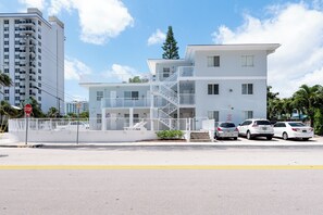 Ein mehrgeschossiges Wohngebäude mit weißer Fassade, mehreren Balkonen und einem verschlossenen Eingang.
