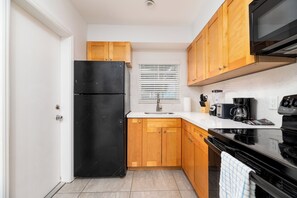Eine kleine Küche mit Holzausstattung, einem schwarzen Kühlschrank, einer Mikrowelle und einer Kaffeemaschine.