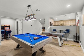 Ein Billardtisch in einem Raum mit Küche und Spielautomaten.