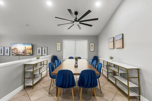 Een vergaderzaal met een lange tafel, blauwe stoelen, een plafondventilator en kunstwerken aan de muur.