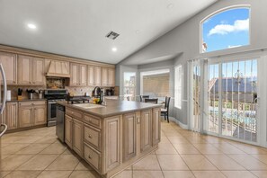 Een ruime keuken met een groot eiland, moderne apparatuur en uitzicht op een zwembad door de schuifdeuren.