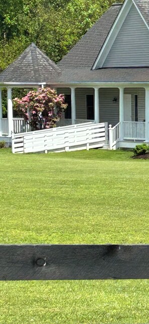 A house with a porch, a fenced yard, and a tree with pink flowers. - Round Hill Retreat-One Bedroom Apartment - Handicap Accessible (Round Hill)