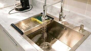 A stainless steel kitchen sink with a modern faucet, a coffee maker, and a green sponge.