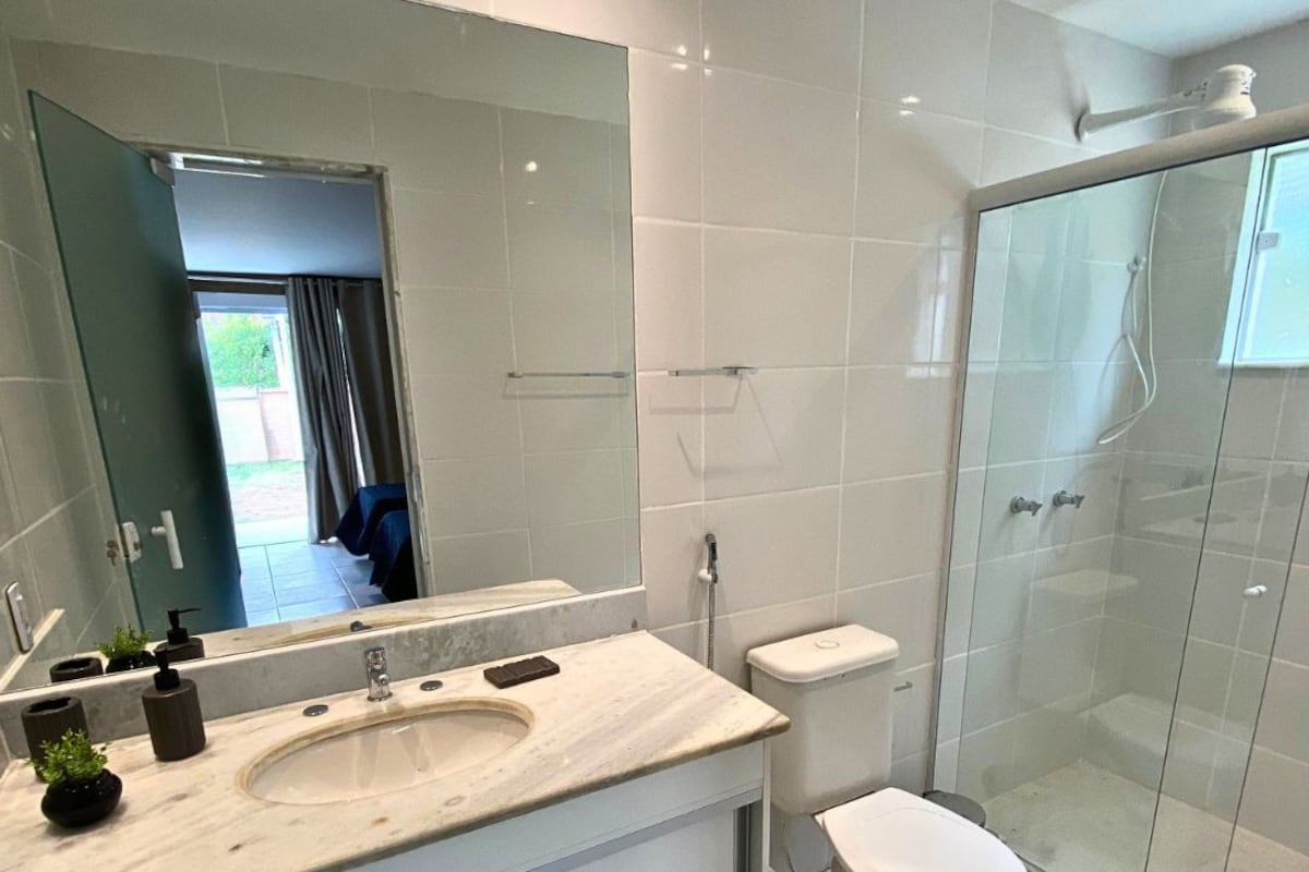 Un baño moderno con un espejo grande, un lavamanos, un inodoro y una ducha con mampara de vidrio.