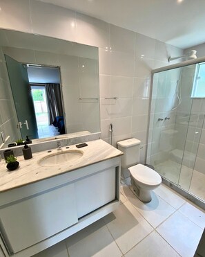 Un baño moderno con un espejo grande, un lavamanos, un inodoro y una ducha con mampara de vidrio.