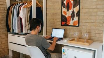 Quarto com escrivaninha branca, laptop, guarda-roupa branco e aparelho de ar condicionado.