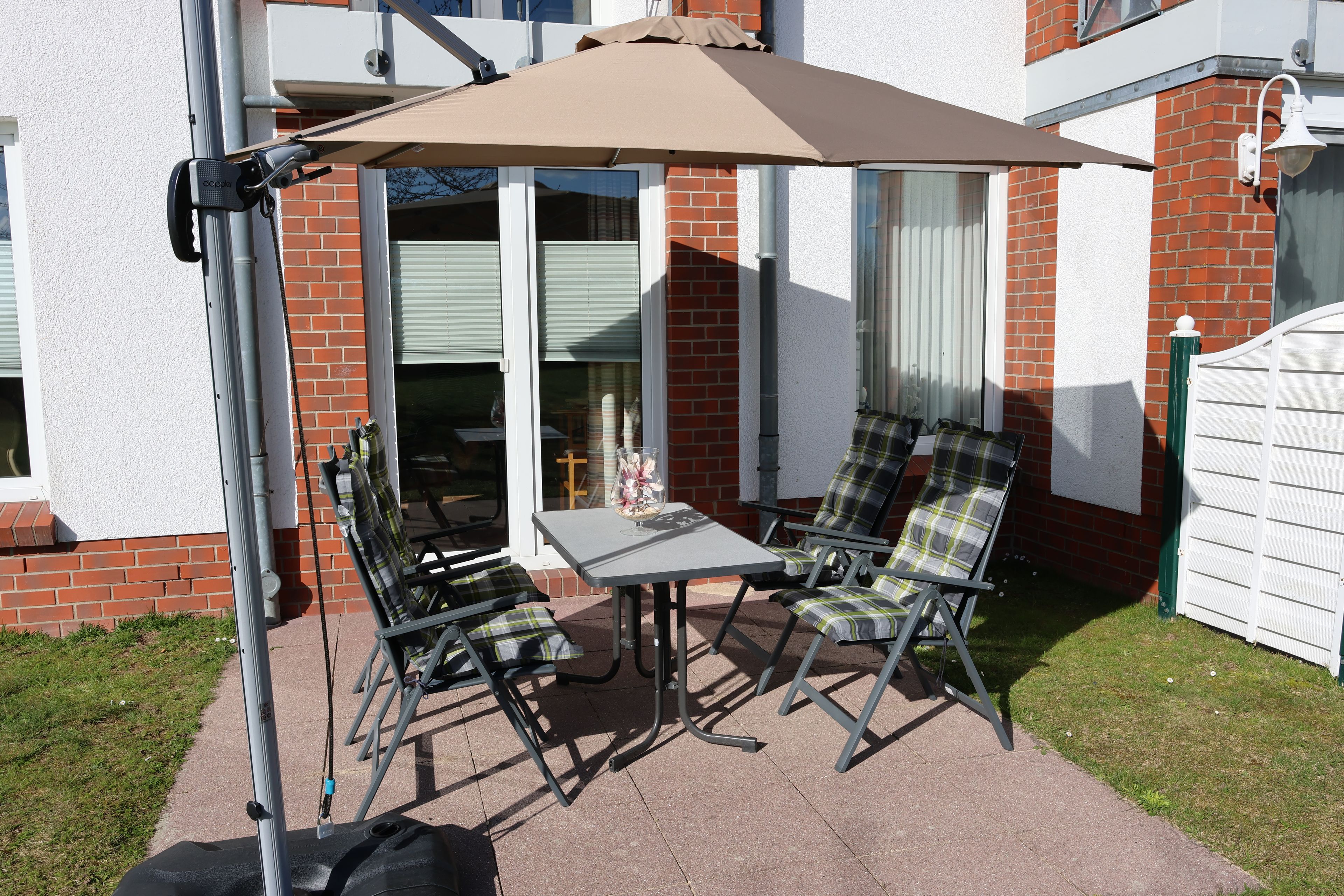 An outdoor patio with a table and two chairs, a patio umbrella, and a brick wall.