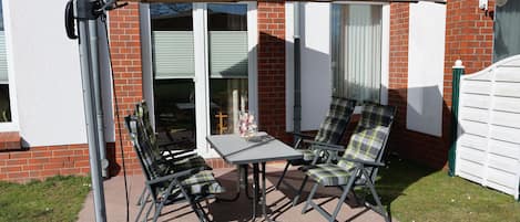 An outdoor patio with a table and two chairs, a patio umbrella, and a brick wall.