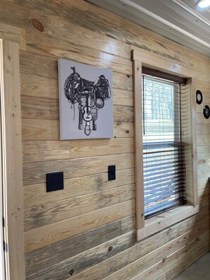 Una pared de madera con un cuadro enmarcado, una ventana con persianas y un interruptor de luz en la pared.