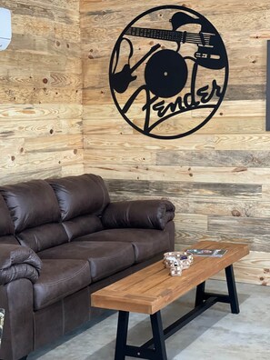 Ein braunes Ledersofa vor einer Holzwand mit Fender-Logo.