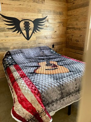 Eine gesteppte Decke mit Gitarrenmuster auf einem Bett in einem Zimmer mit Holzwänden.