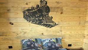 Ein Holzraum mit einem Bett, ausgestattet mit einer detailliert gestalteten, mechanisch inspirierten Tagesdecke und passenden Kissen.