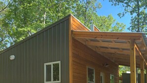Eine Holzhütte mit überdachter Veranda, einem Picknicktisch und zwei roten Stühlen.