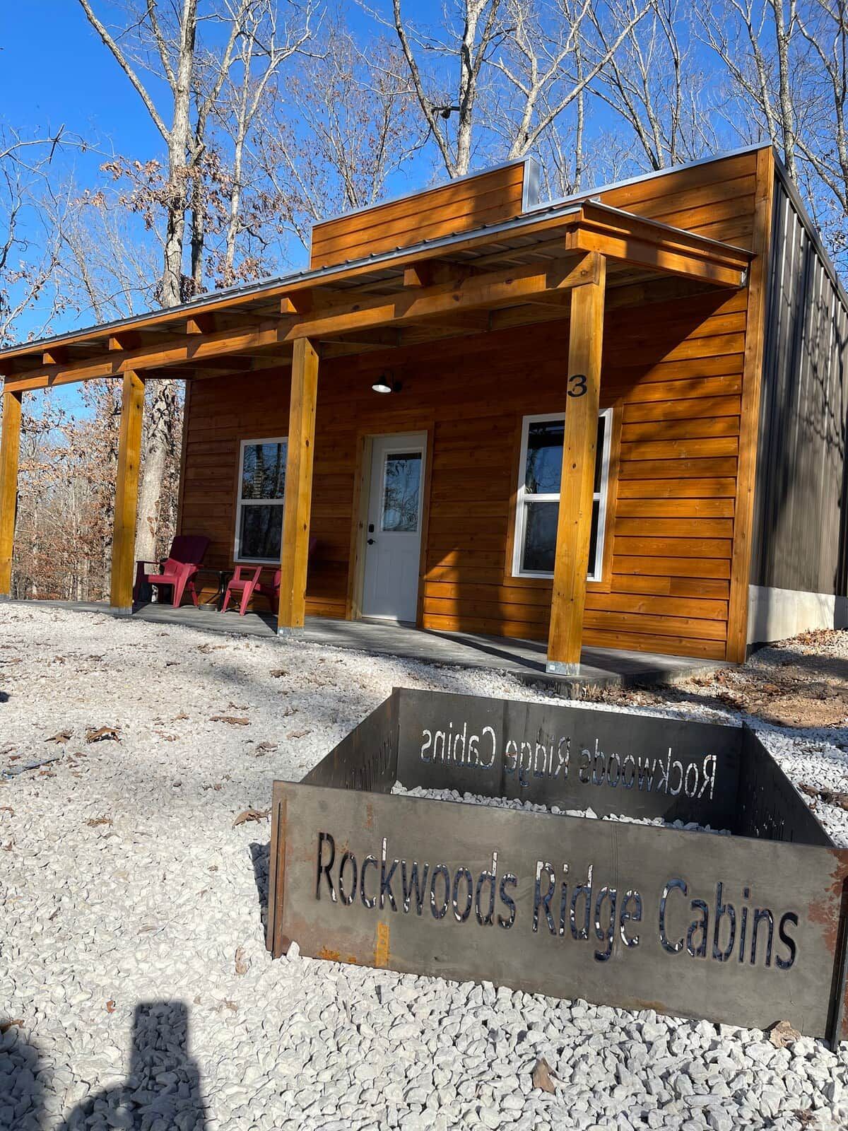 A cabin with a wooden exterior, a porch with chairs, and a sign indicating 'Rockwoods Ridge Cabins'.