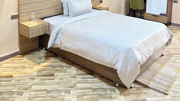 A hotel room with a large bed, wooden headboard, two bedside tables, a water bottle, a painting, and a mirror on the wall. - Harar Palace Hotel (Harar)