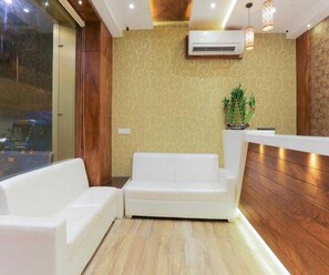 A reception area with a white sofa, wooden paneling, and a potted plant. - Collection O Chena Creek Godbandar (Mumbai)