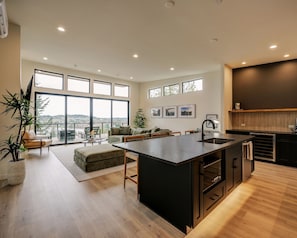 A spacious kitchen with a large island, modern appliances, and a view through large windows.