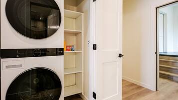 A laundry room with two front-loading washing machines and a door leading to a hallway.