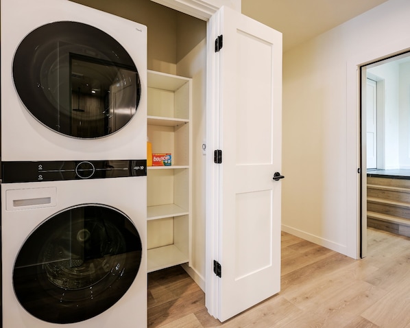 A laundry room with two front-loading washing machines and a door leading to a hallway.