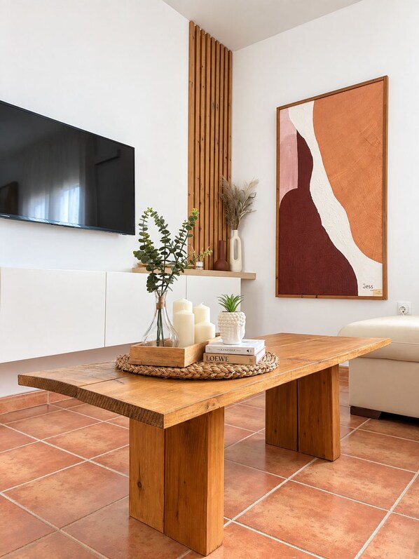 A modern kitchen with a wooden dining table, white cabinetry, a flat-screen TV, and a large abstract painting.