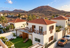 A residential area with white buildings, red-tiled roofs, and a mountain in the background.