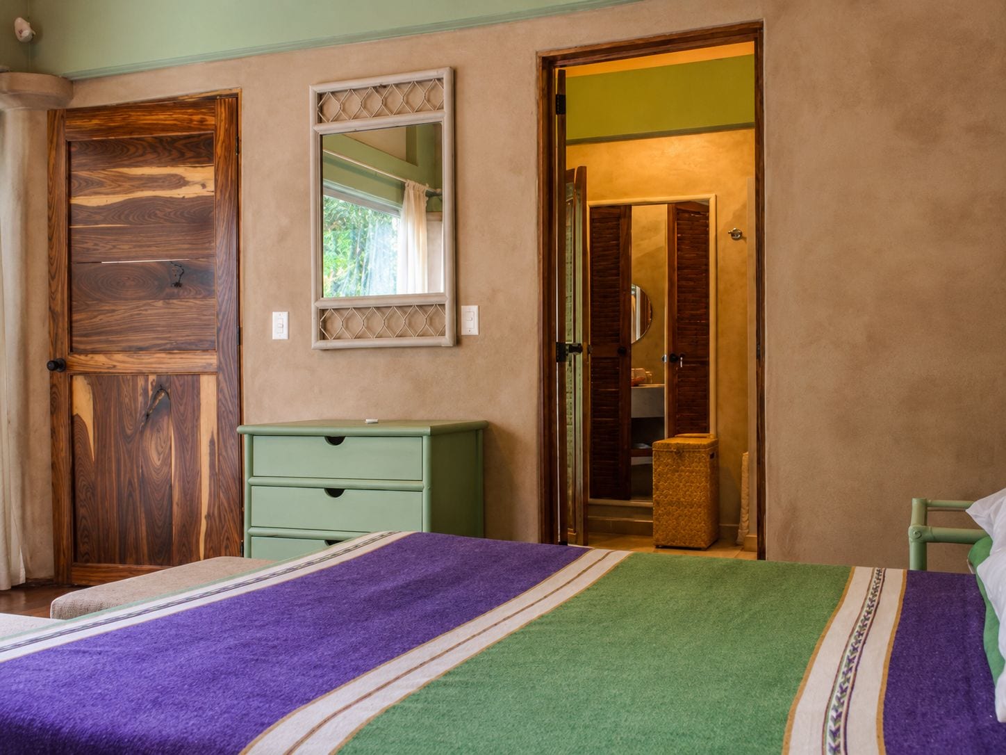 Une pièce comprenant un lit, une commode verte, un miroir et une porte donnant sur une salle de bain.