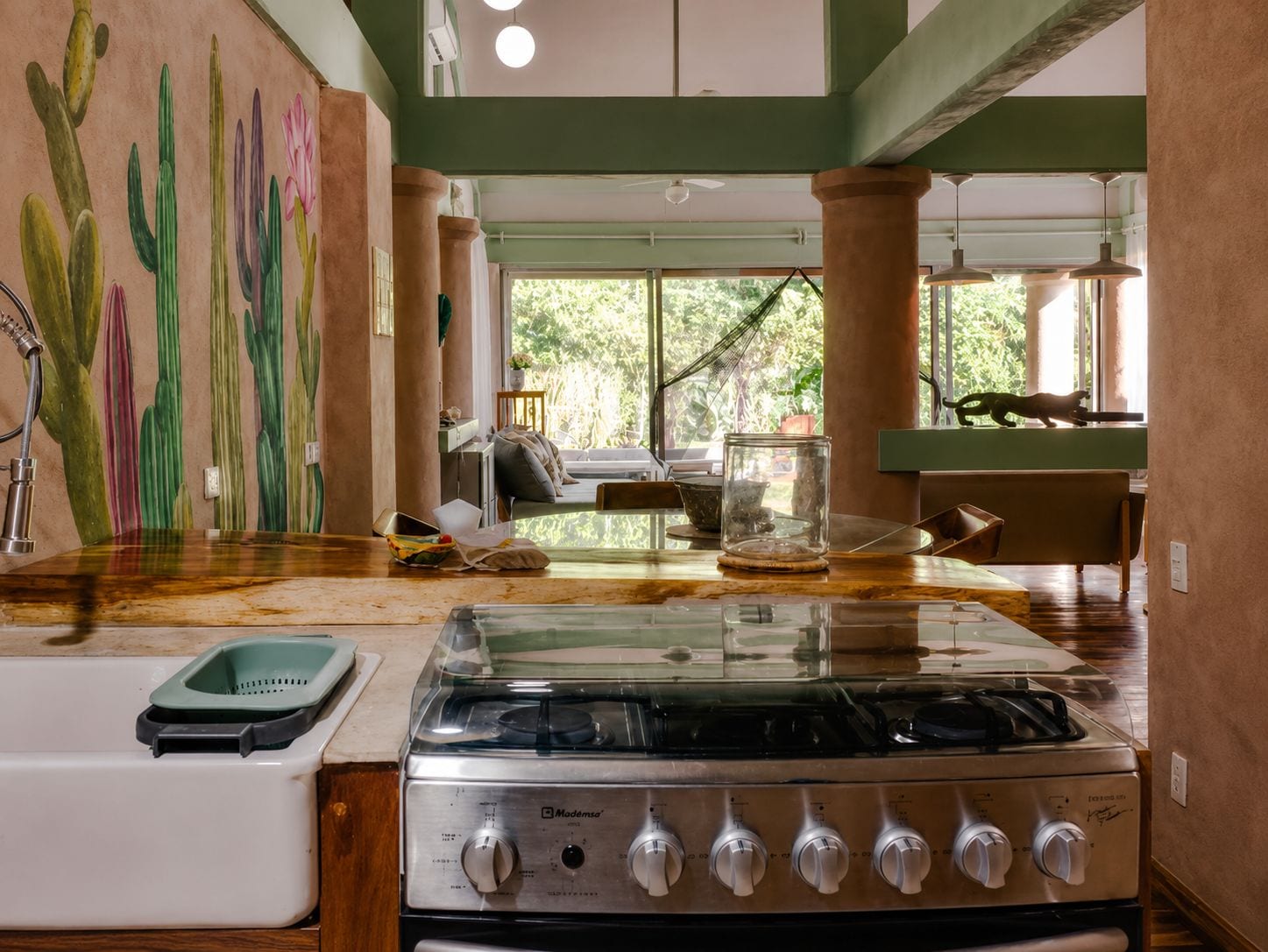 A kitchen with a gas stove, a sink, and a mural of cacti on the wall.