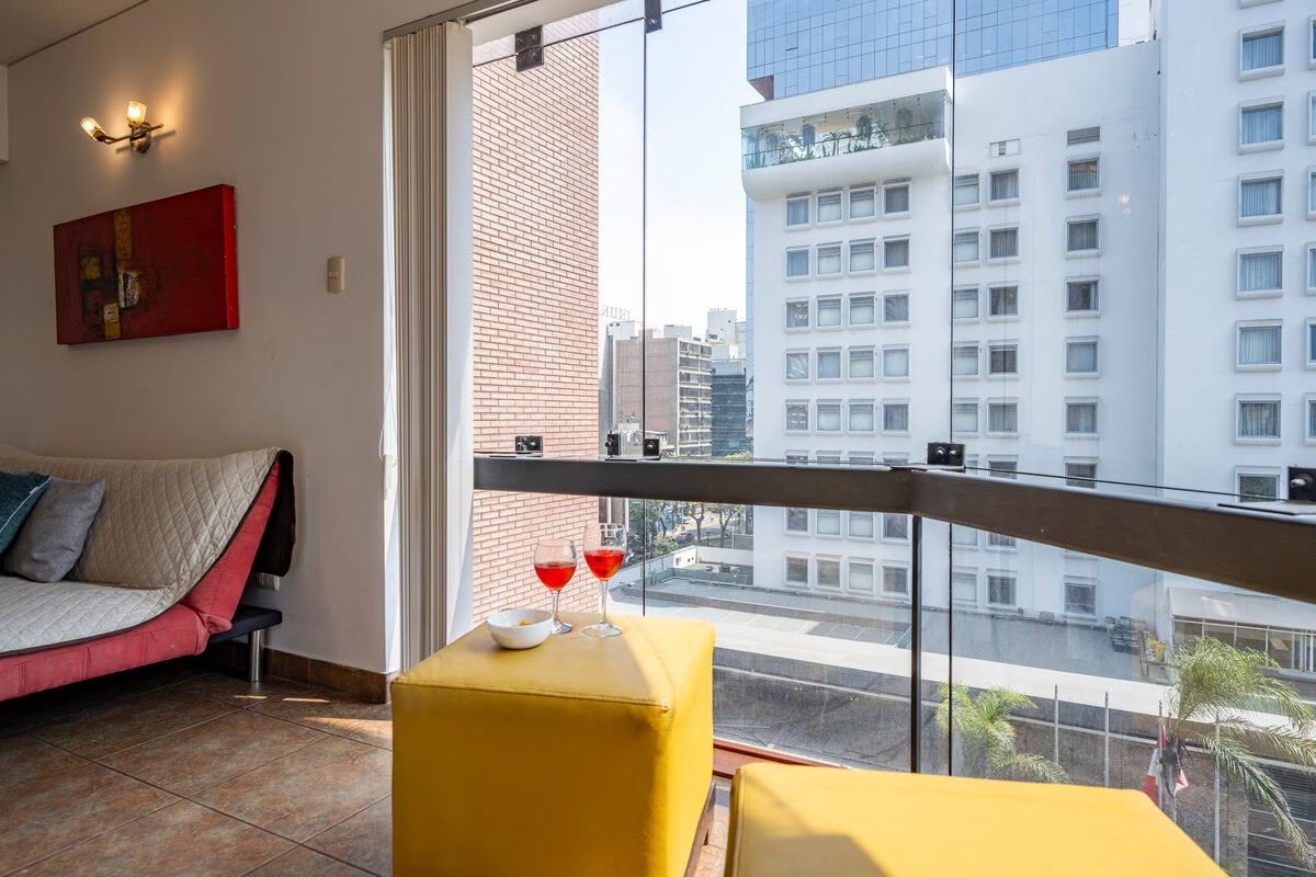 Une chambre d’hôtel moderne avec un lit, un pouf jaune et un balcon offrant une vue sur la ville.