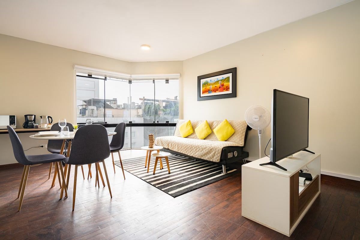 A modern living room with a sofa, a flat-screen TV, and a dining area with chairs and a table.