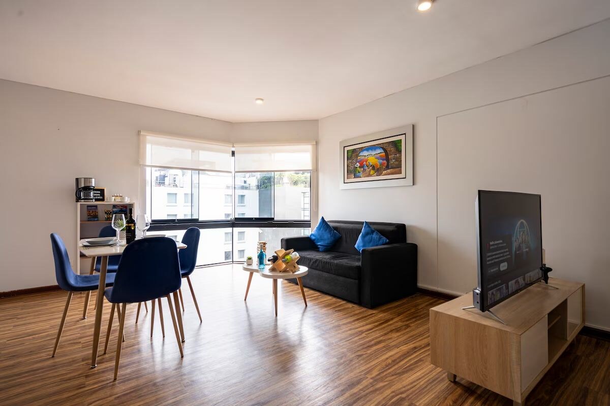 A modern living room with a black sofa, blue chairs, a coffee table, a flat-screen TV, and a painting on the wall.