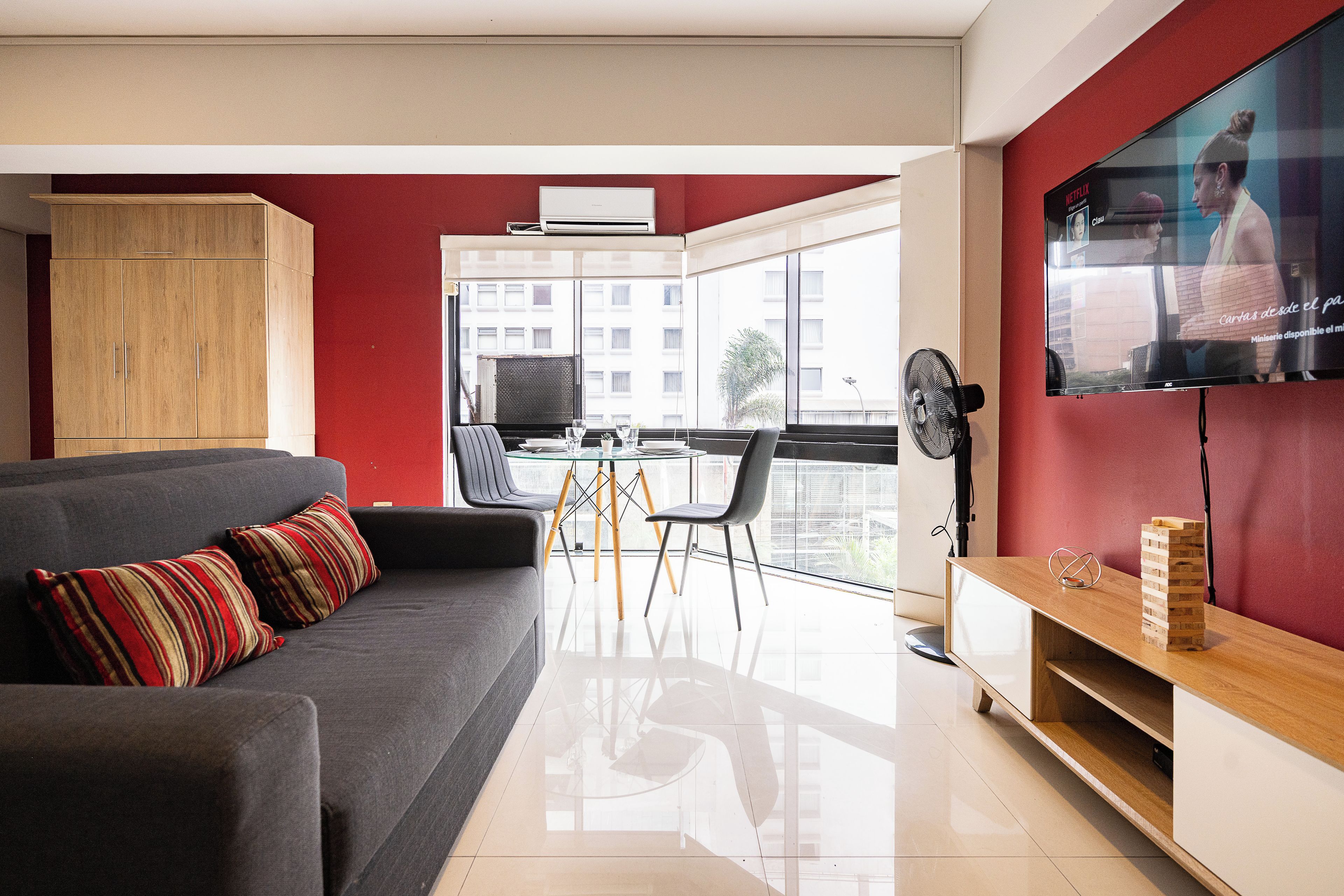 Ein modernes Wohnzimmer mit einem grauen Sofa, einem Holzkabinett und einem Glastisch mit Stühlen.