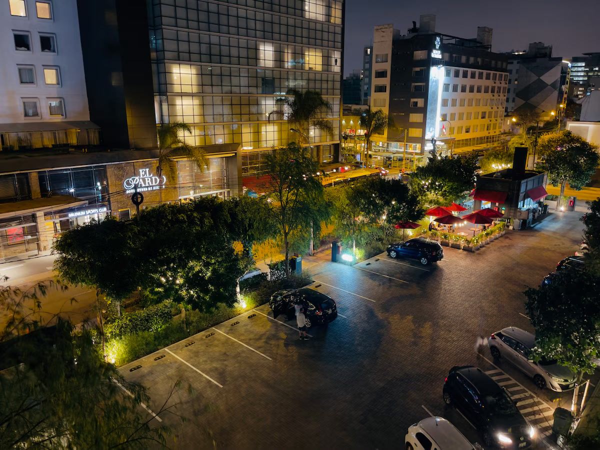 Un estacionamiento con varios autos, un edificio con fachada de vidrio y un letrero que dice 'EL PARD'.