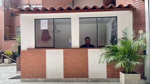 Un espace d’accueil avec une personne debout derrière un comptoir, une plante en pot et un sol carrelé.