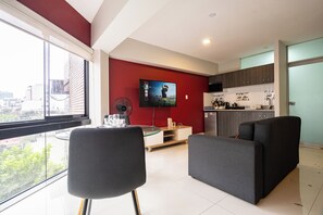 A modern living room with a large TV, a dining area, and a kitchen. - Chateau Studios by Vibrant (Miraflores)