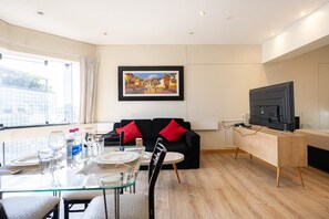 Una sala de estar moderna con comedor, un sofá negro y cojines rojos, un televisor de pantalla plana y un cuadro en la pared.