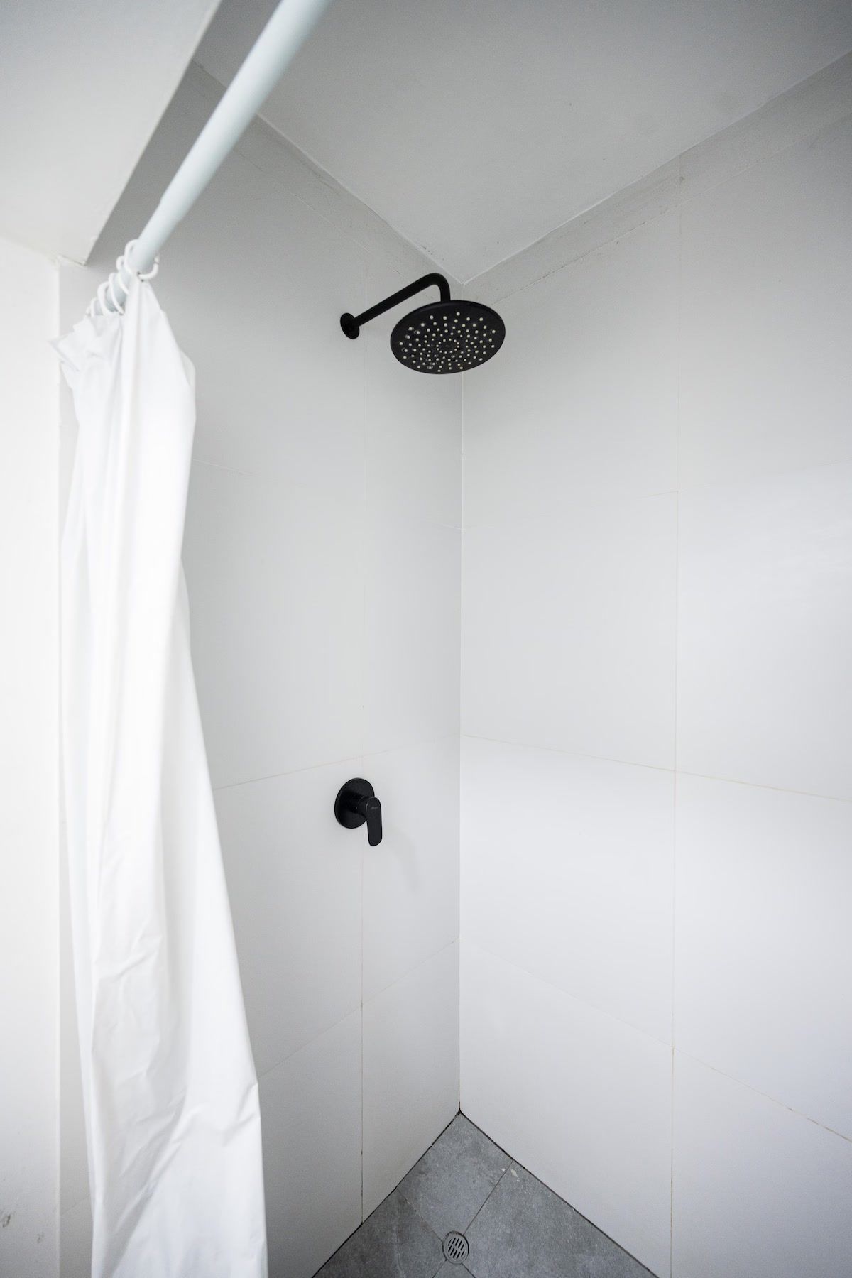 Ducha con cabezal de ducha manual negro y cortina blanca.