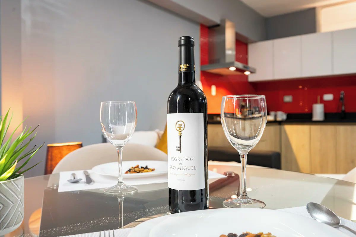 Una botella de vino con etiqueta, dos copas de vino vacías y una mesa de comedor con un plato blanco y una cuchara.